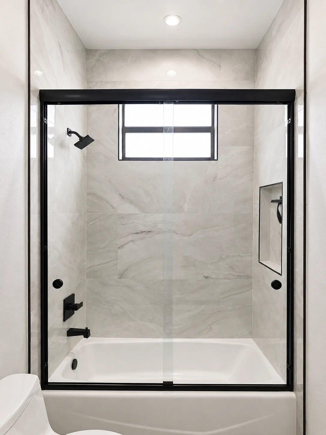 Matte black framed sliding shower door over a white bathtub with marble-look tile in a Sarasota guest bathroom